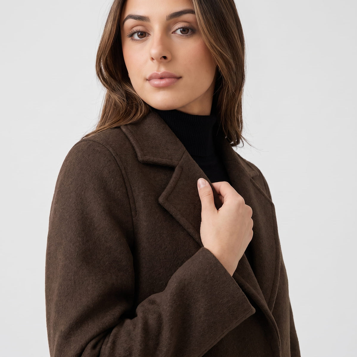 Model holding the lapel of a coffee brown coat, close-up side angle