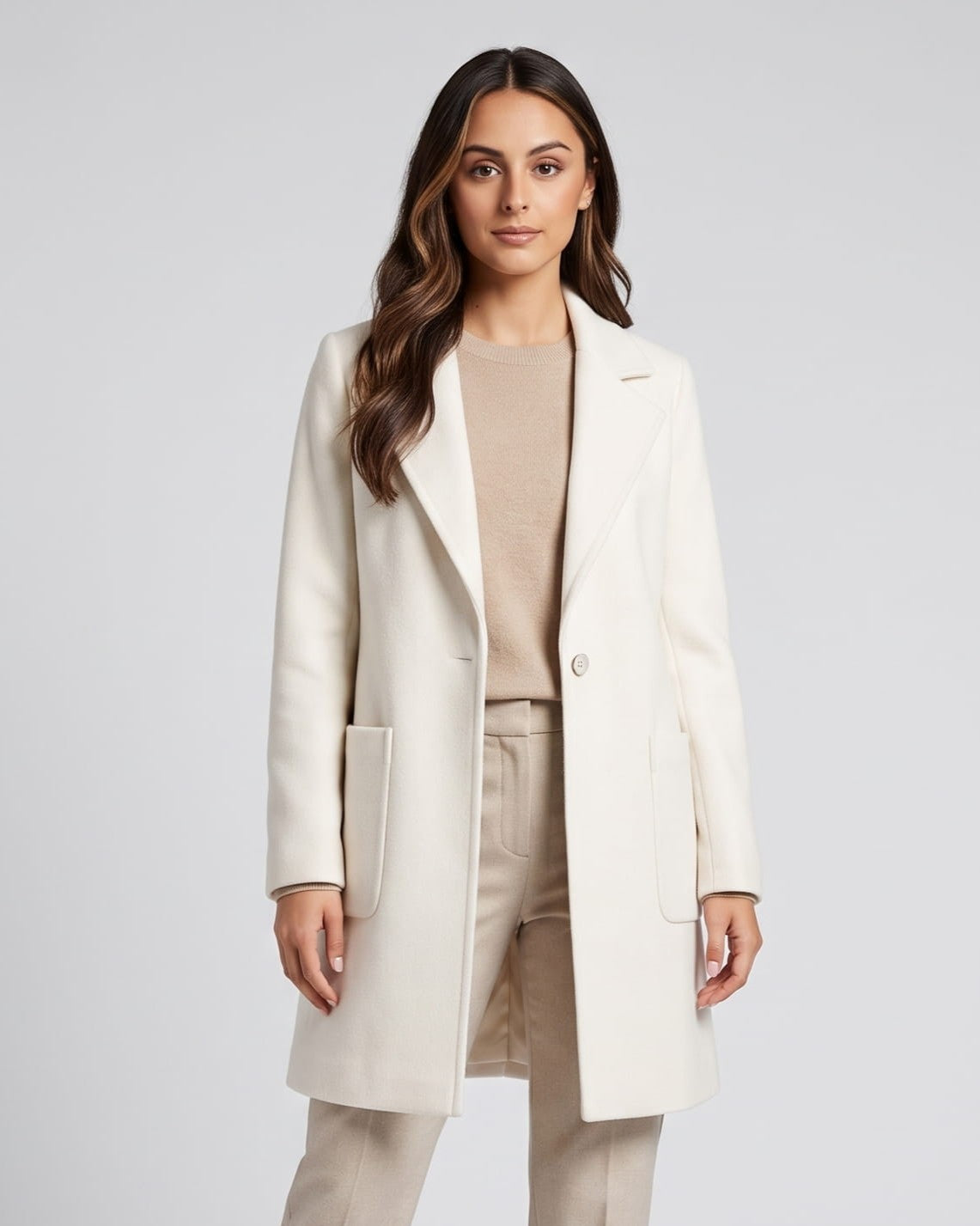 Front view of cream coat worn open over a beige top and trousers