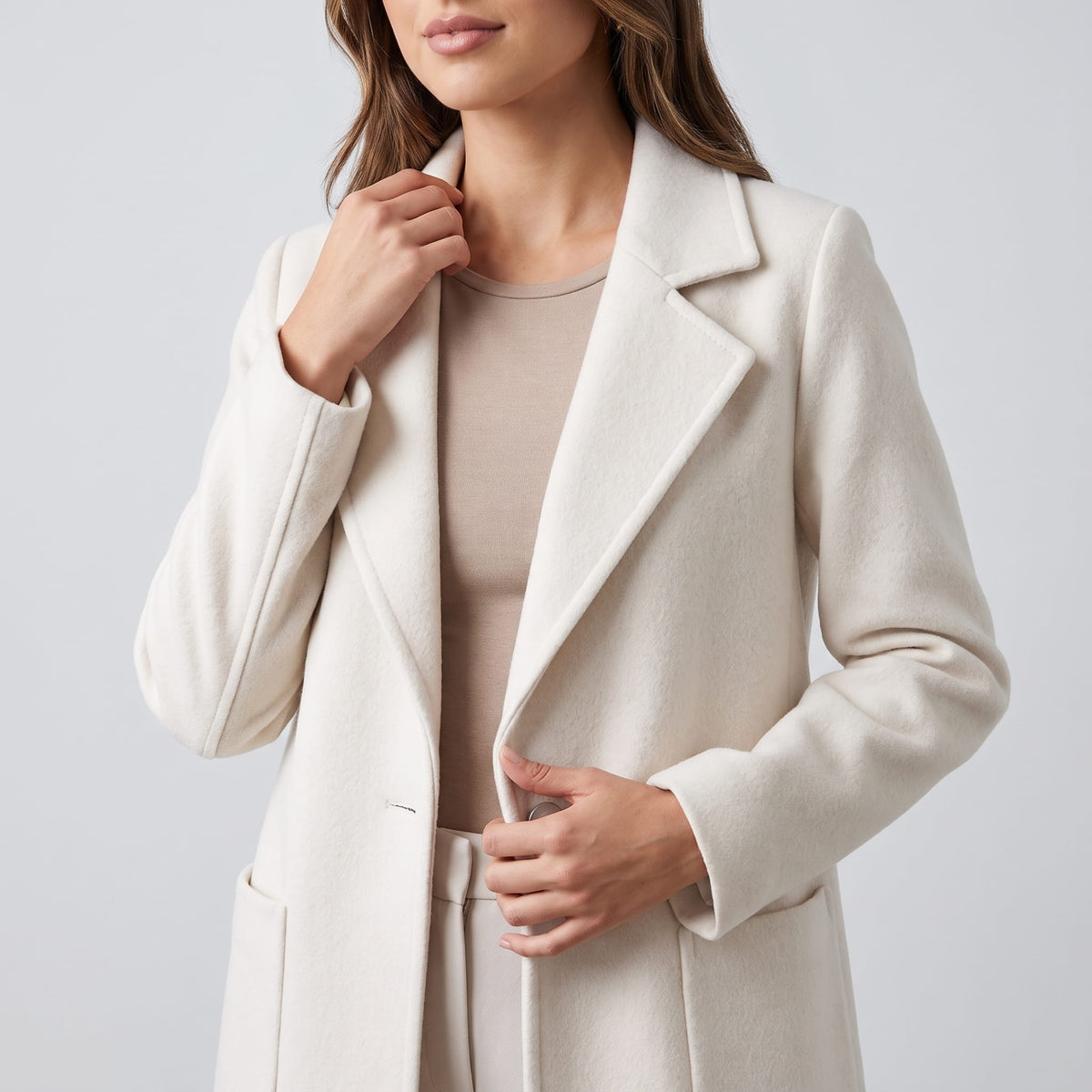 Close-up of cream coat lapel held open by the model's hand