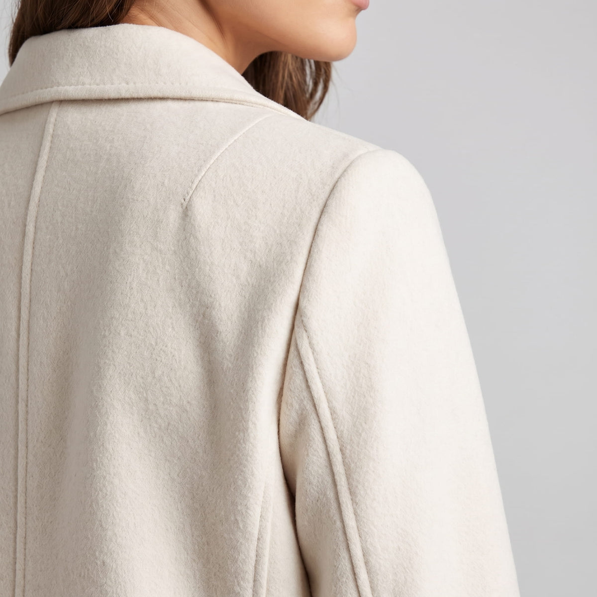 Detail of cream coat shoulder and collar seam from a rear angle
