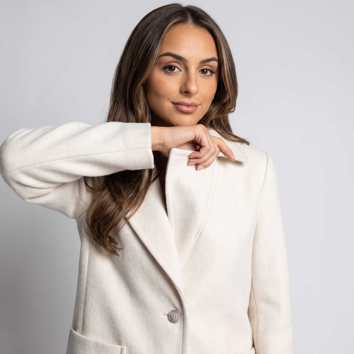 Model raising her arm to show the cream coat sleeve and button front