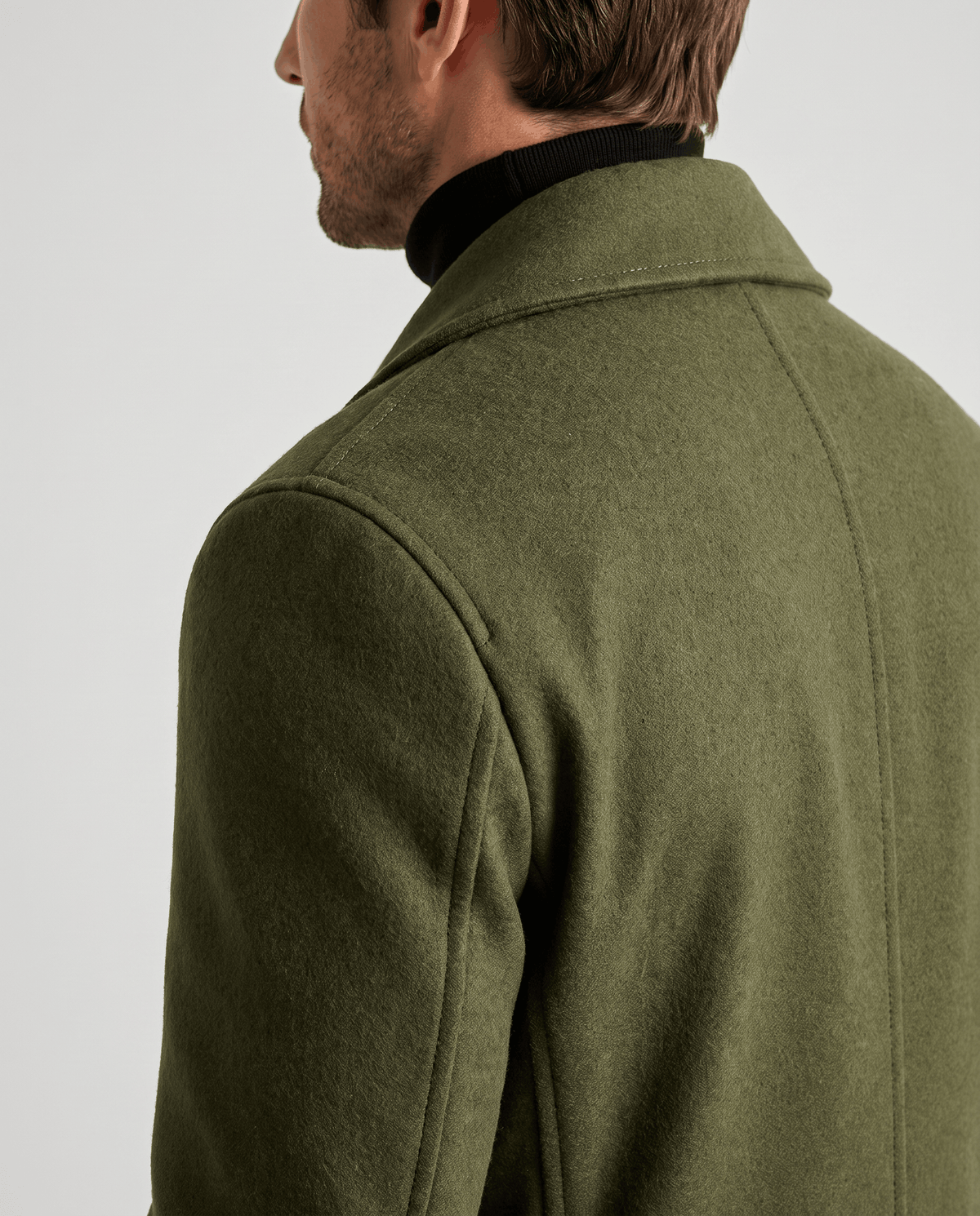 Back shoulder and collar detail of an olive green wool coat worn over a black turtleneck