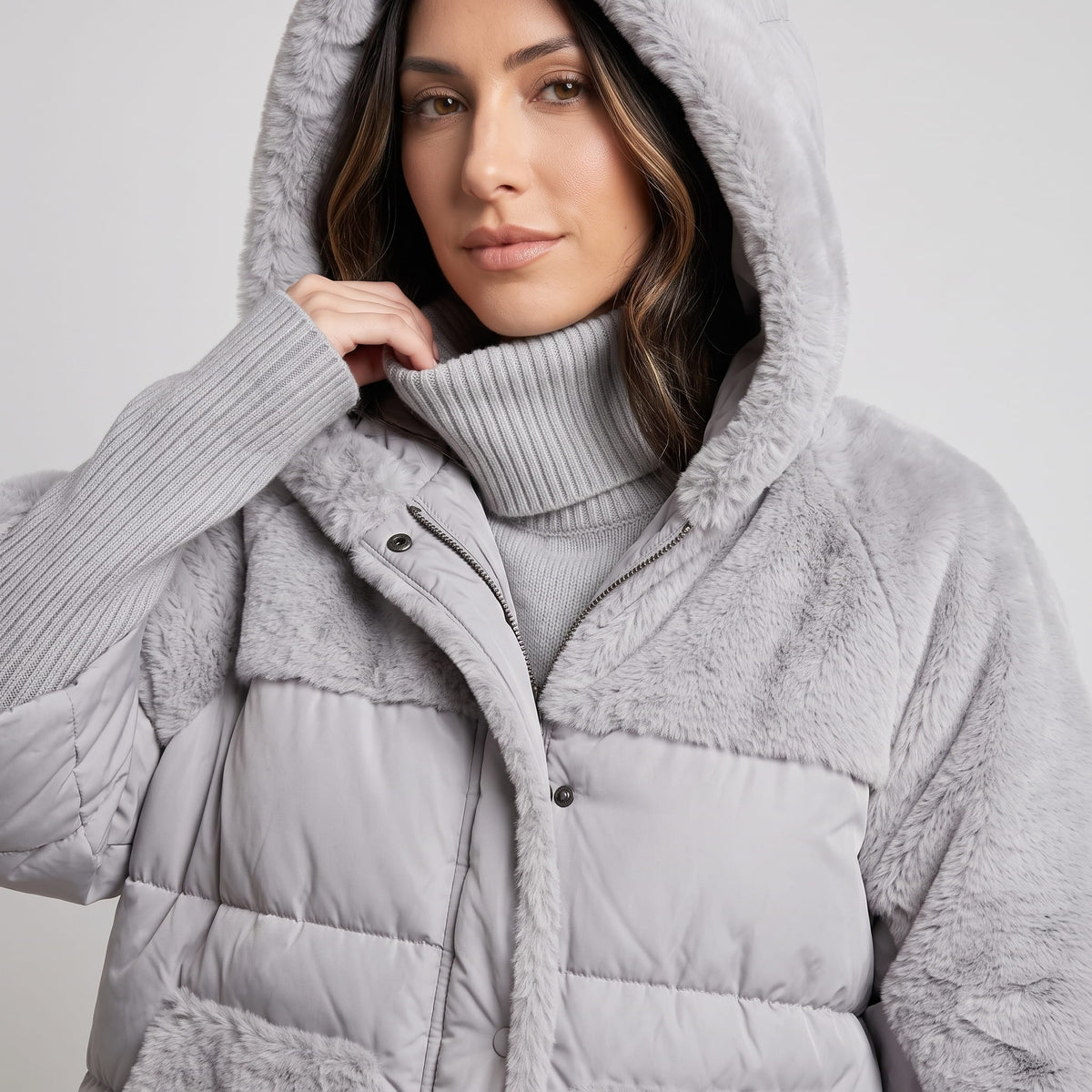 Model holding the raised hood of a gray plush and quilted parka