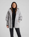 Woman in gray oversized hooded puffer parka with plush panels over dark trousers