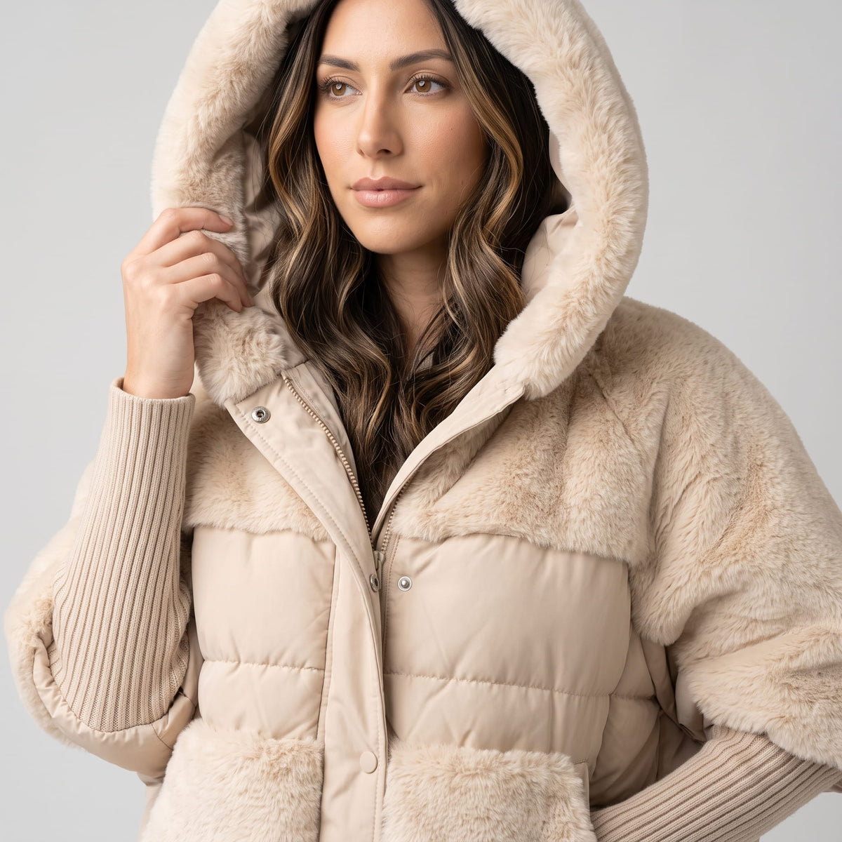 Model holding the plush hood of a light beige quilted parka