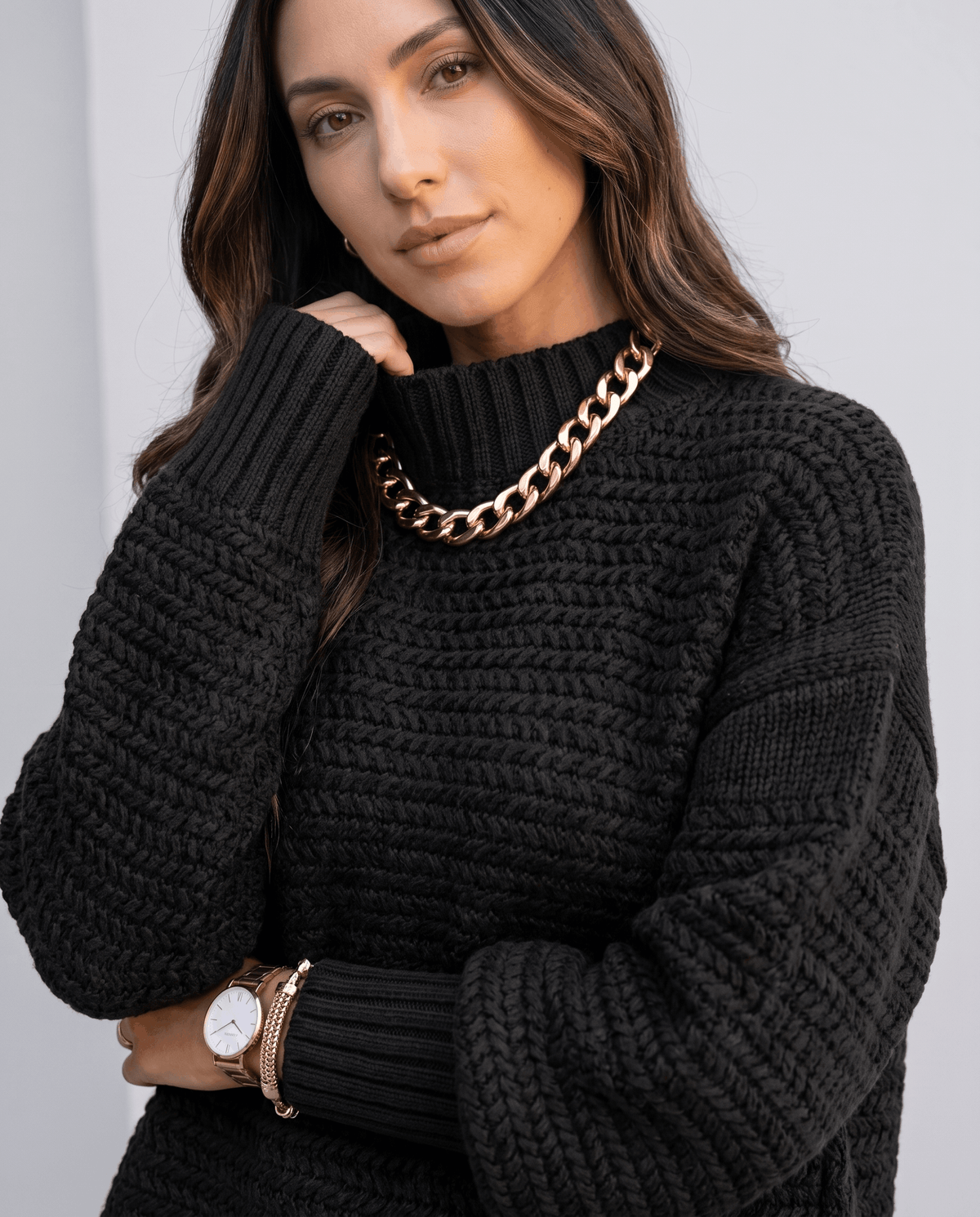 Close-up of black chunky knit mock neck with gold chain necklace and watch