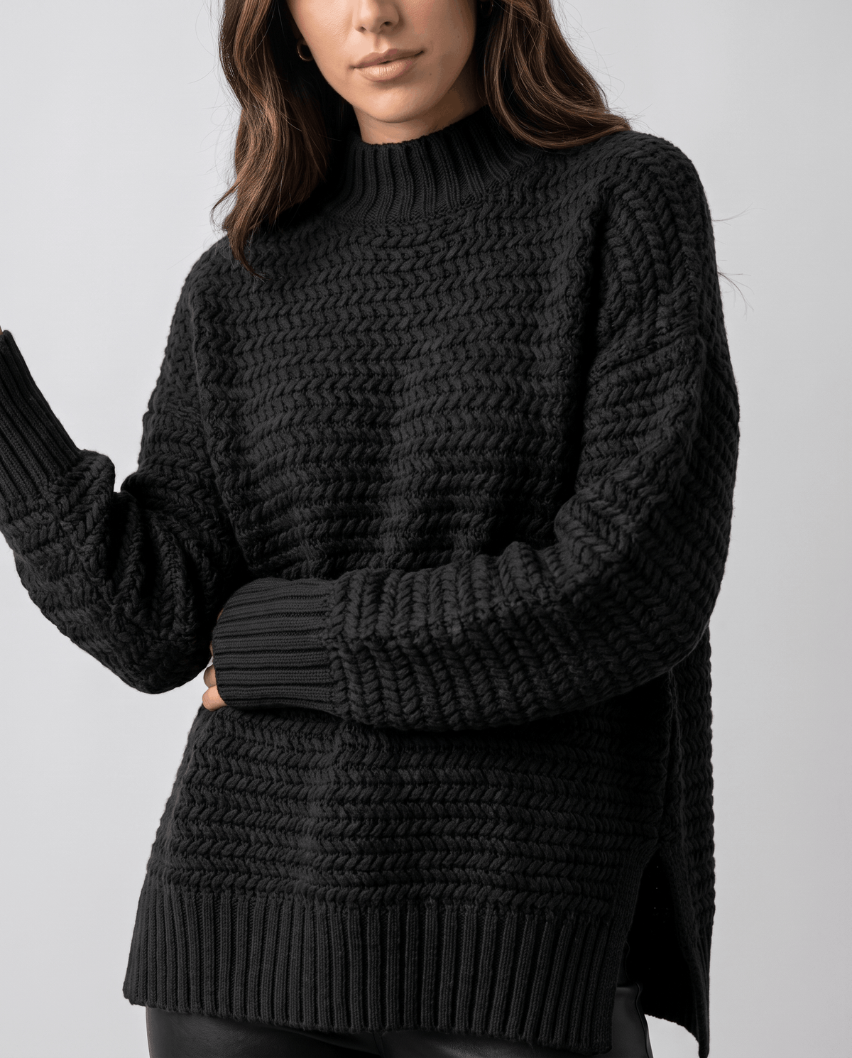 Side view of black textured pullover with side slit hem and raised arm