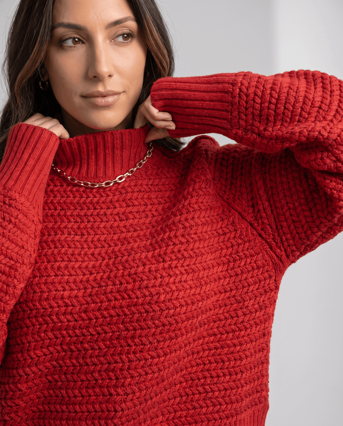 Close-up of model touching the ribbed mock neck of a red chunky knit