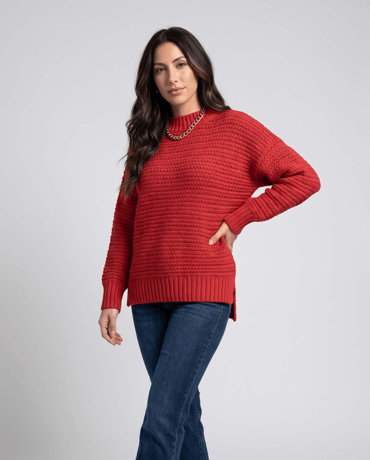 Woman wearing a red oversized mock neck sweater with dark jeans and gold necklace