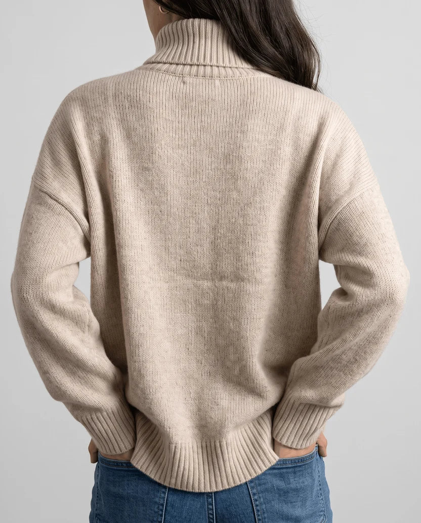 Back view of beige turtleneck sweater with ribbed hem, worn with jeans
