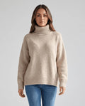 Woman in oversized turtleneck sweater with dropped shoulders, beige wool knit, front view with jeans