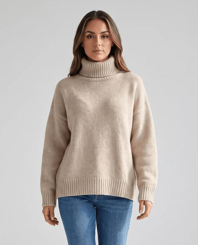 Woman in oversized turtleneck sweater with dropped shoulders, beige wool knit, front view with jeans