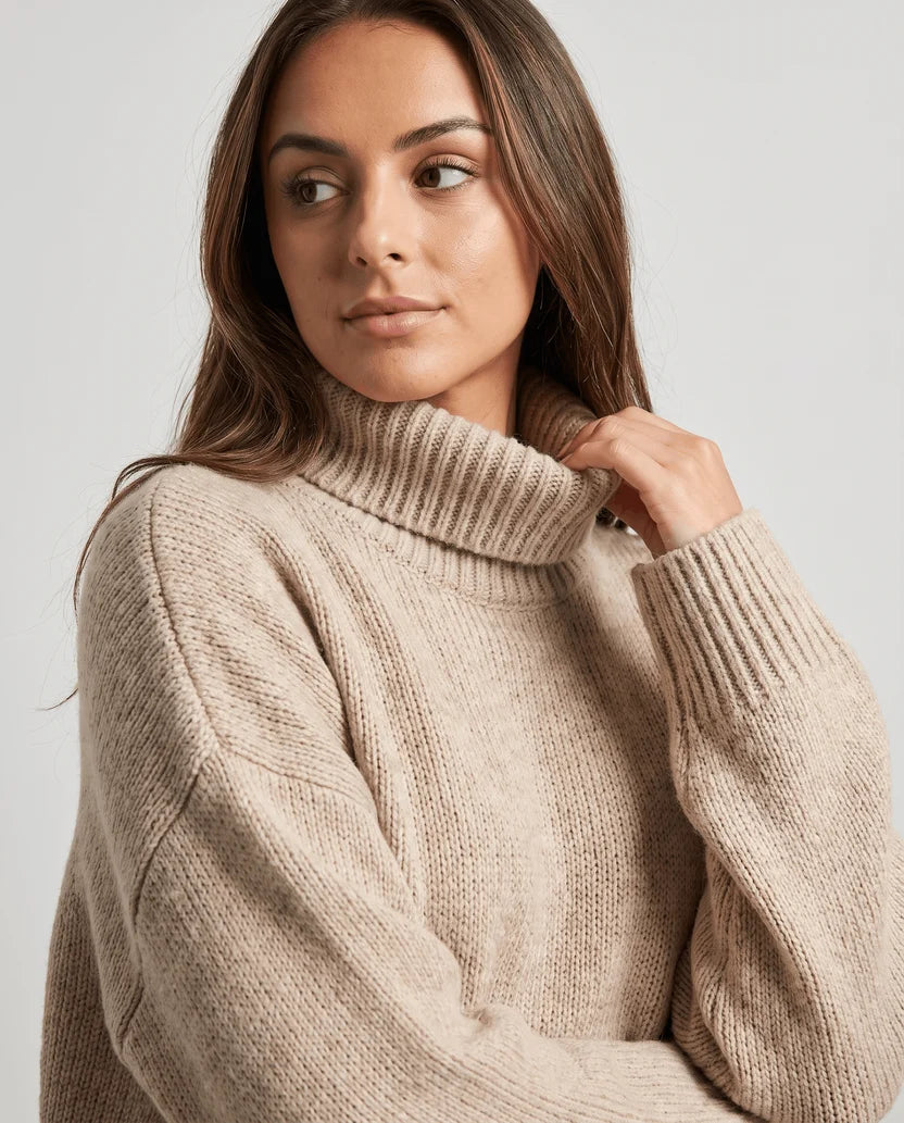 Close-up of model in dark beige sweater with hand at the tall ribbed collar