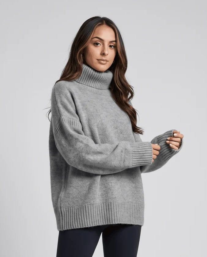 Model in gray turtleneck sweater with raised hand, loose sleeves and relaxed drape