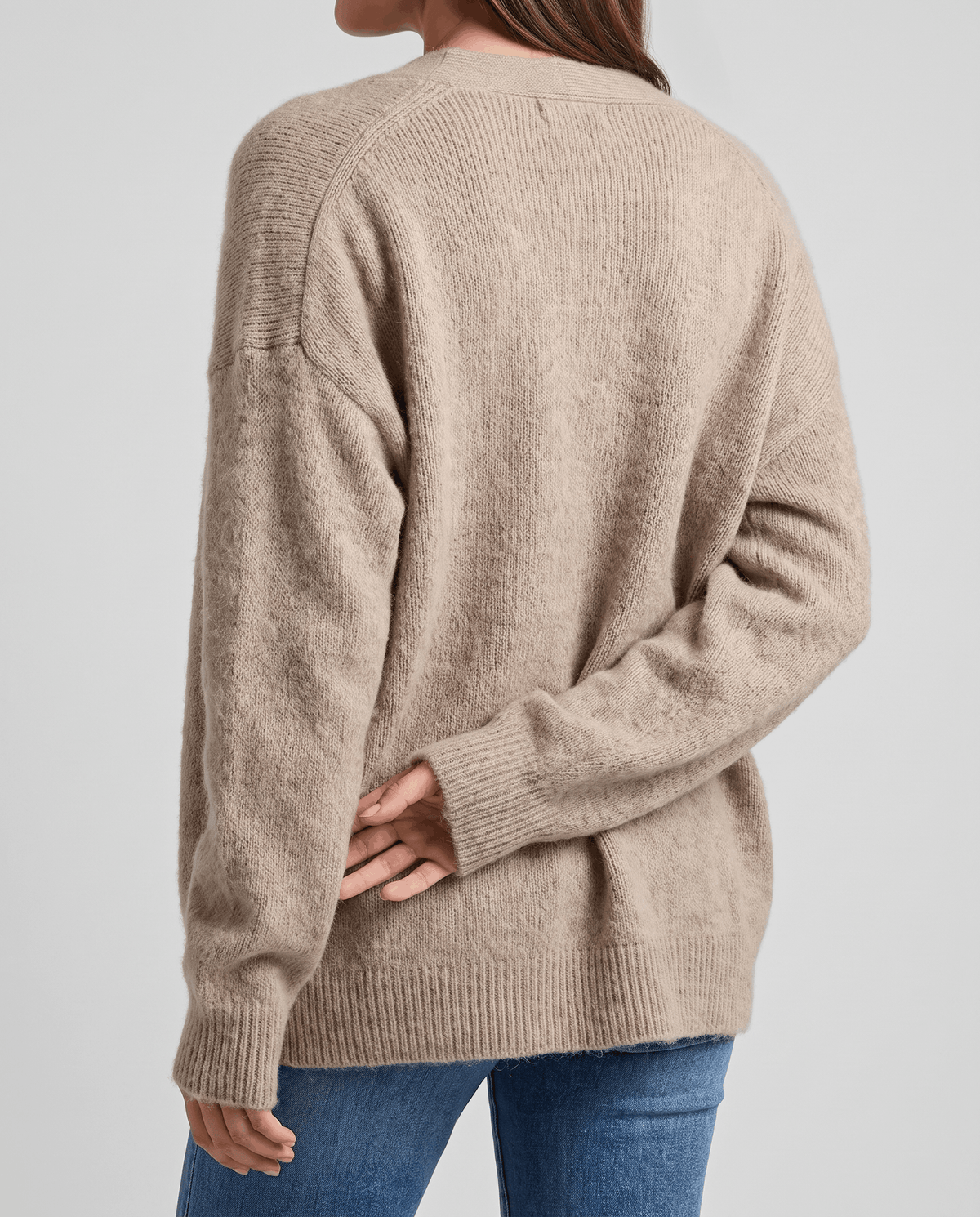 Back view of the beige cardigan worn with jeans showing its roomy oversized shape