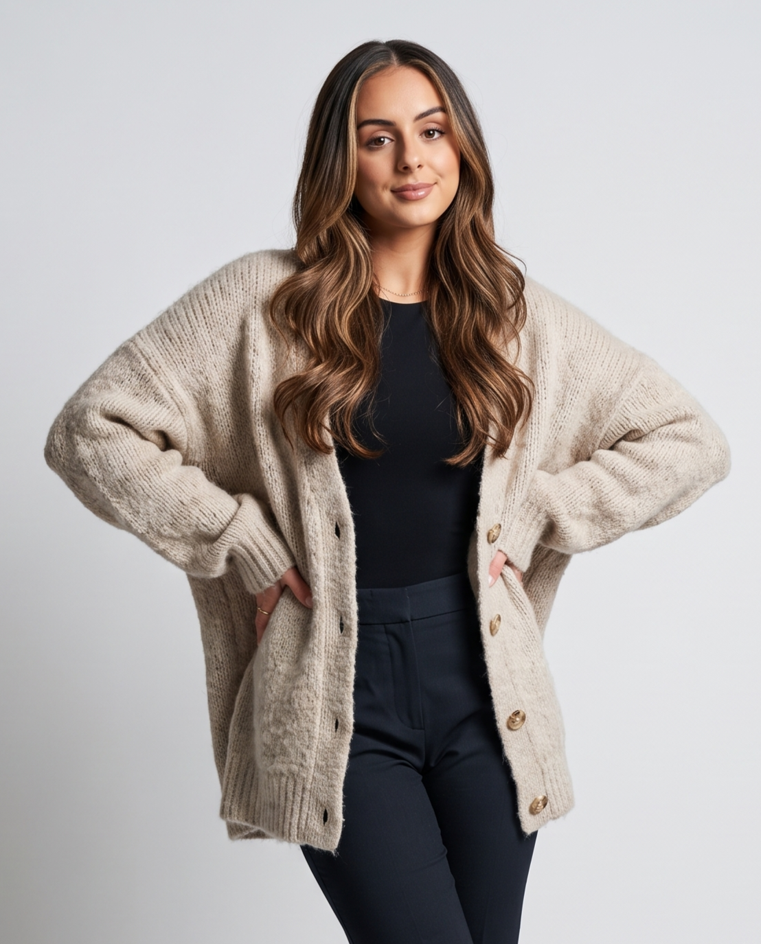 Beige cardigan with hands in pockets over a black top and navy pants