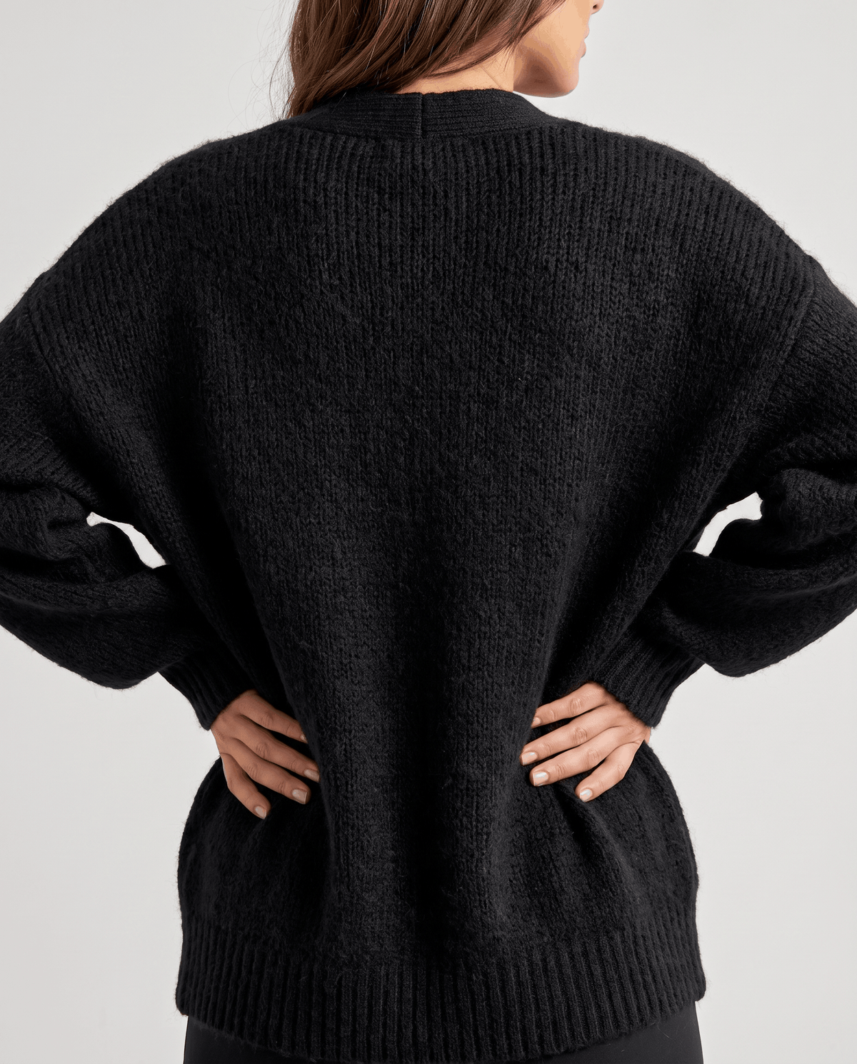 Back view of the black cardigan worn with hands on hips showing its wide cut