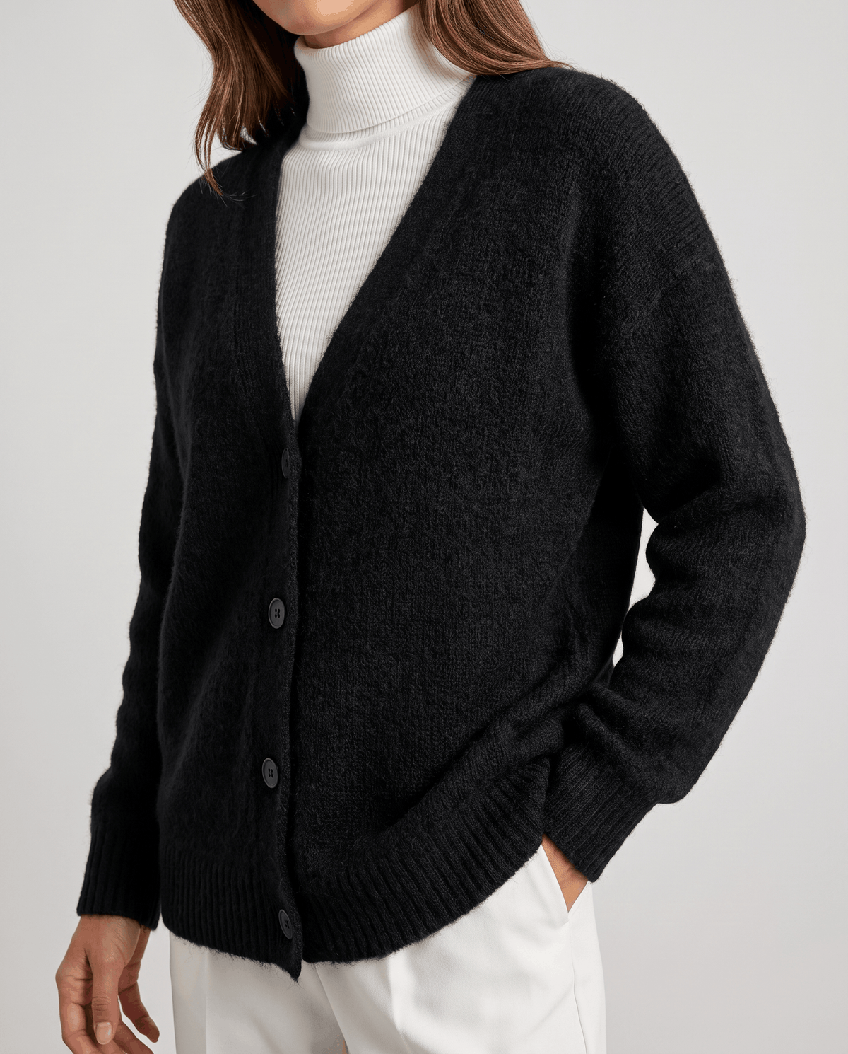 Close-up of the black cardigan front buttons and ribbed hem over white pants