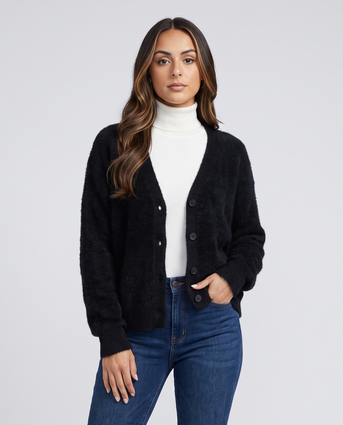 Black cardigan over a white turtleneck with blue jeans and a hand in pocket