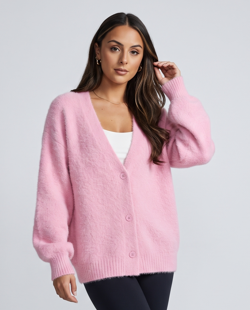Pink cardigan worn open over a white top with a hand at the hair