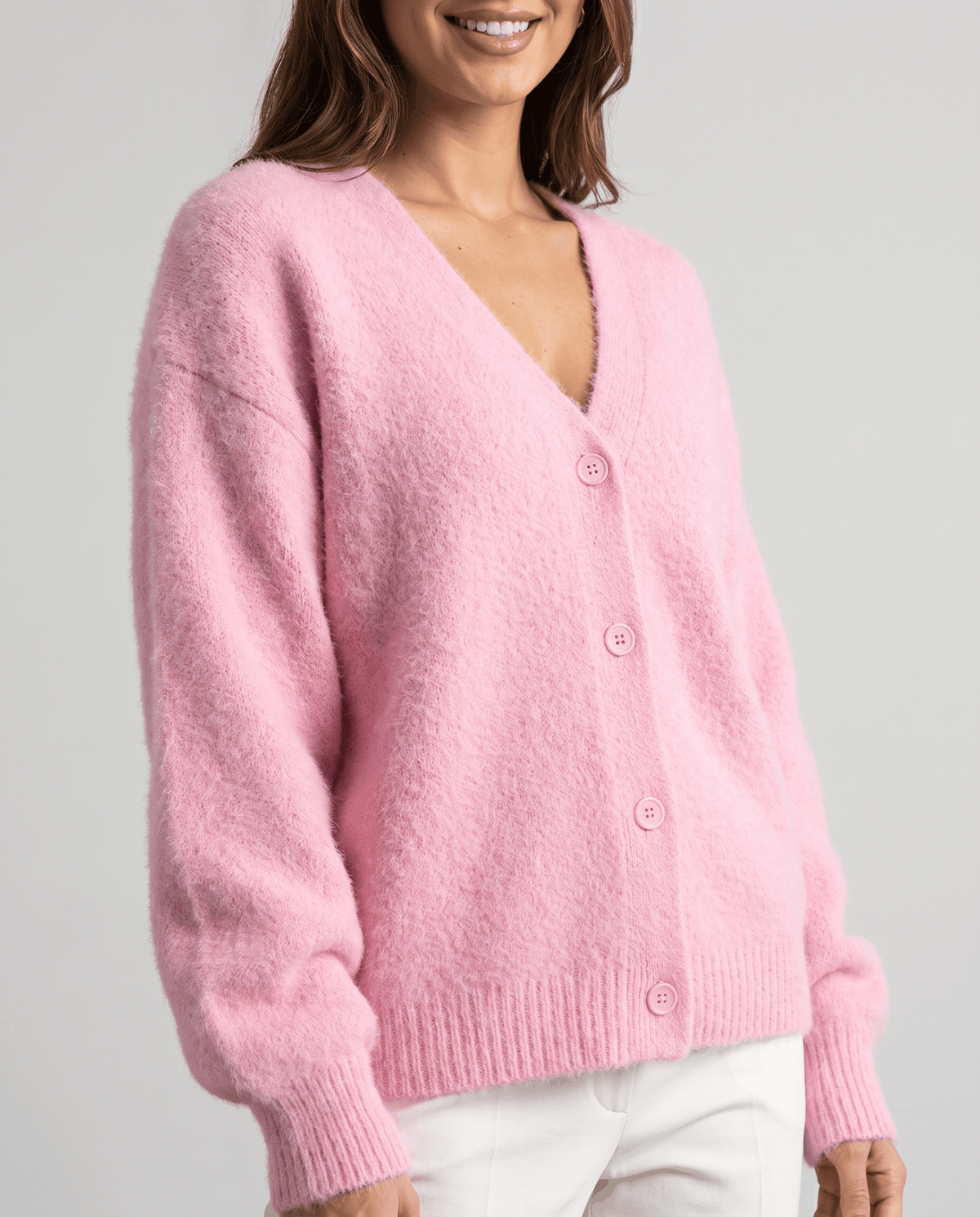 Three-quarter view of the pink cardigan worn over white trousers