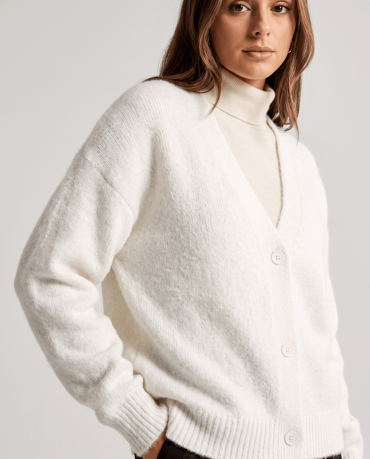 Close-up of the white cardigan worn open over a white turtleneck with visible buttons