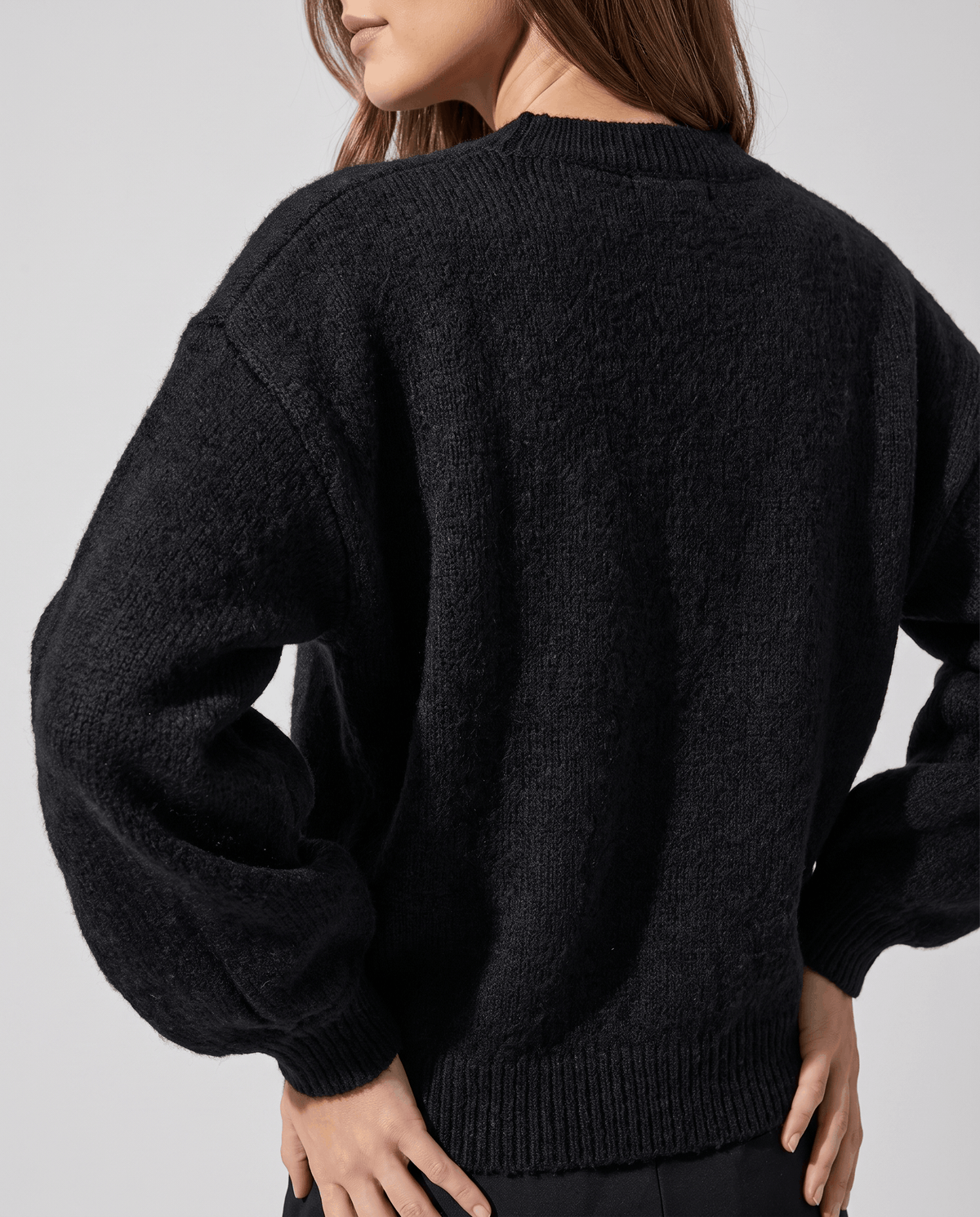 Back view of the black cardigan showing roomy balloon sleeves and ribbed cuffs