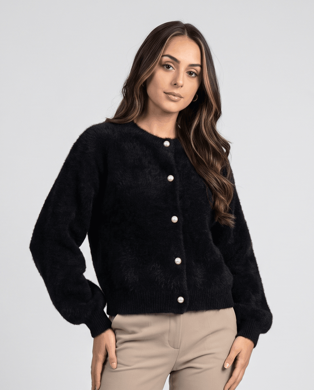 Black cardigan buttoned with beige trousers and a hand on the hip