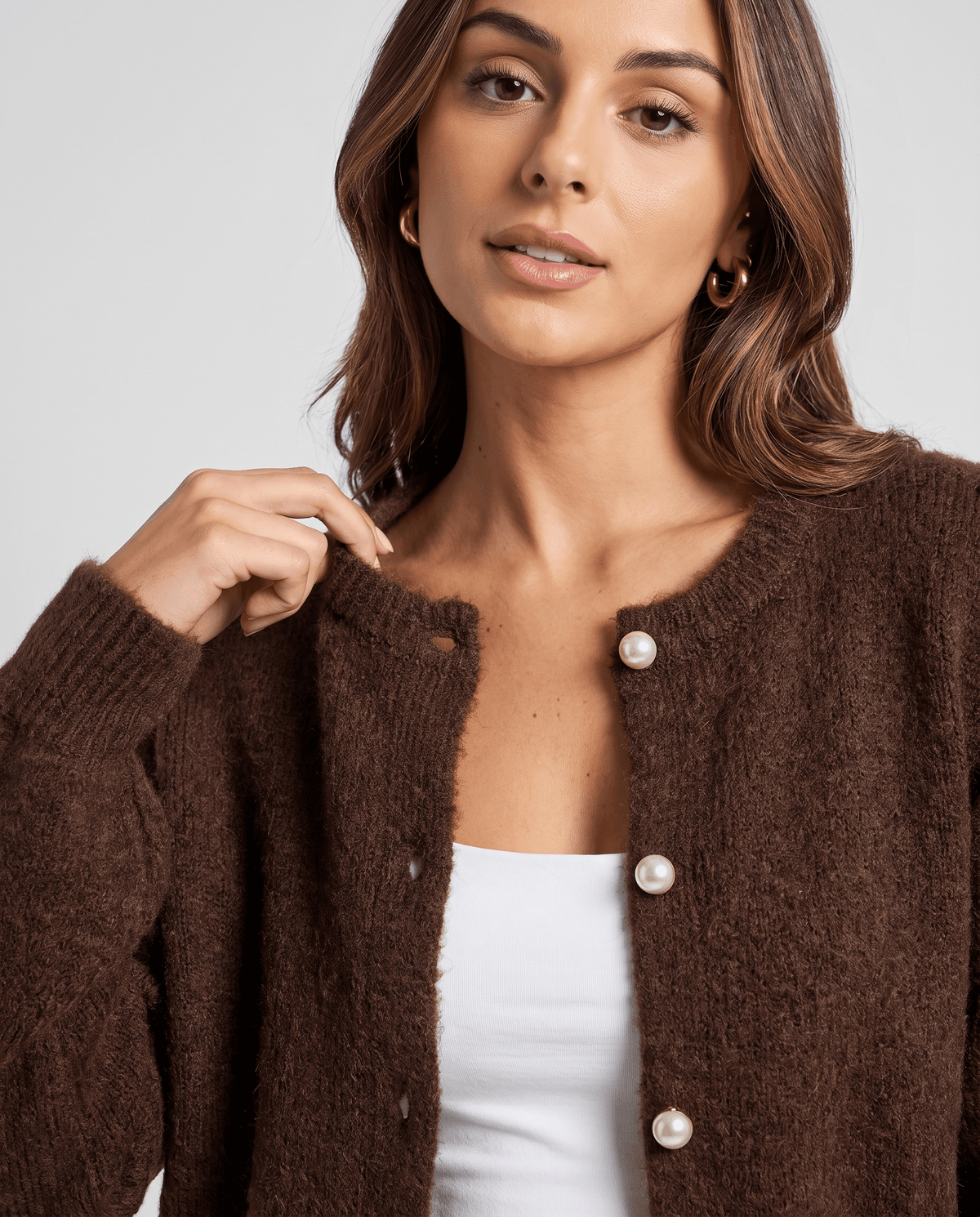 Close-up of the brown cardigan's crew neck and pearl buttons over a white tank