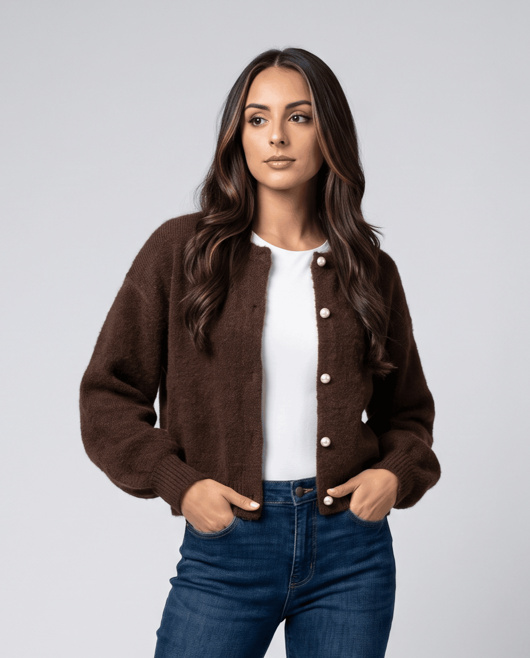 Brown cardigan open over a white tee with hands in jean pockets