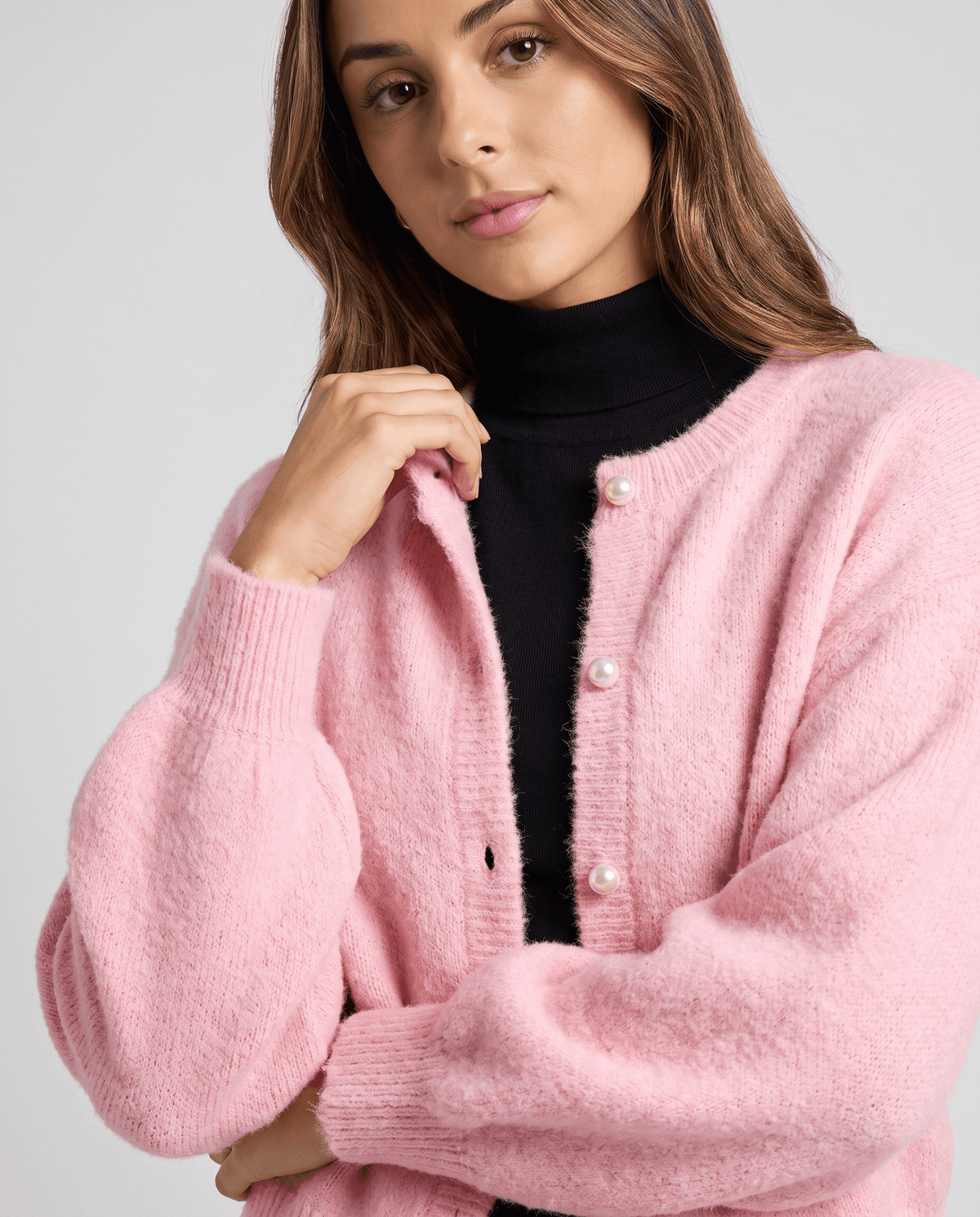 Close-up of the pink cardigan's crew neck and pearl buttons over a black turtleneck