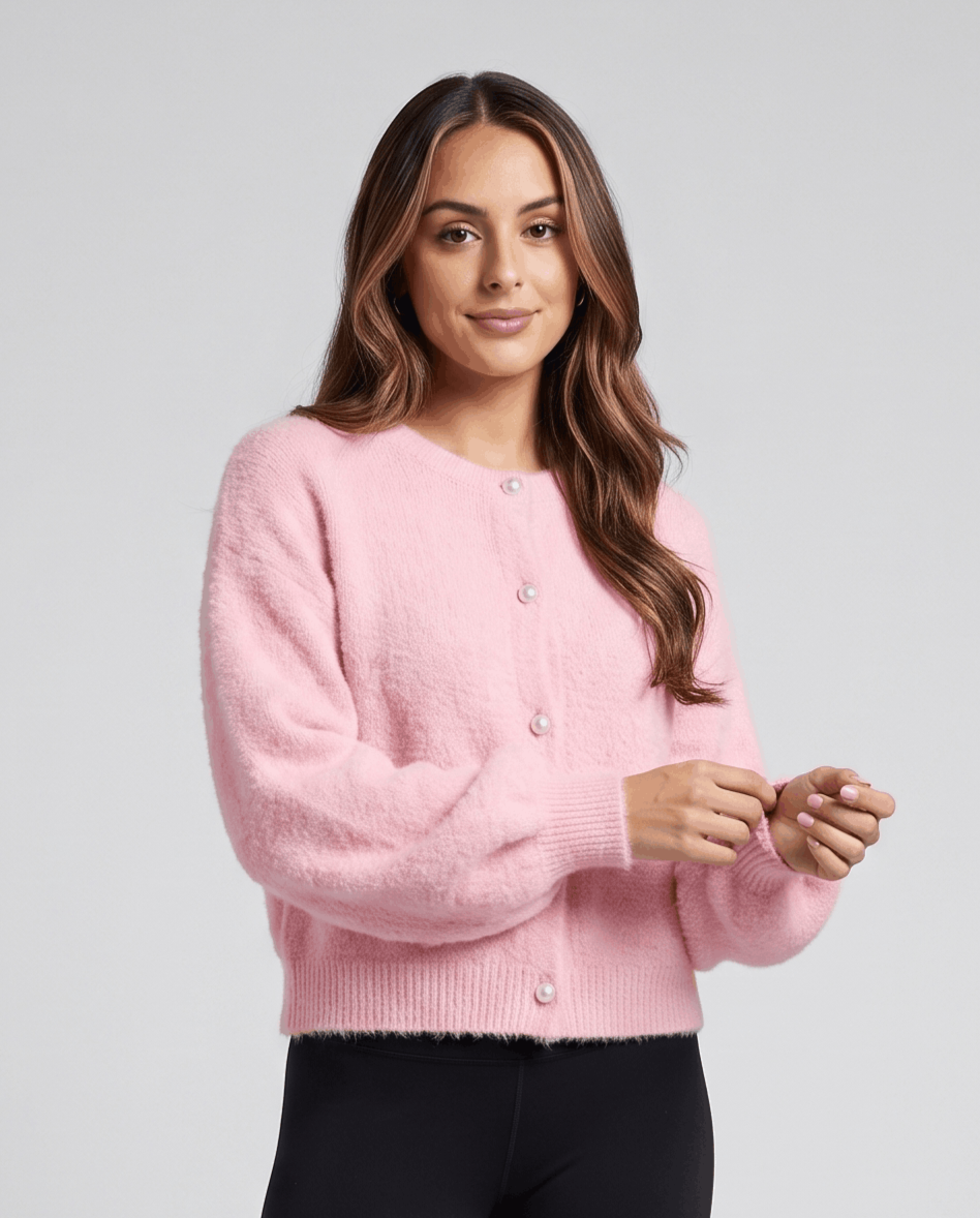 Pink cardigan buttoned with black pants and hands together at the waist