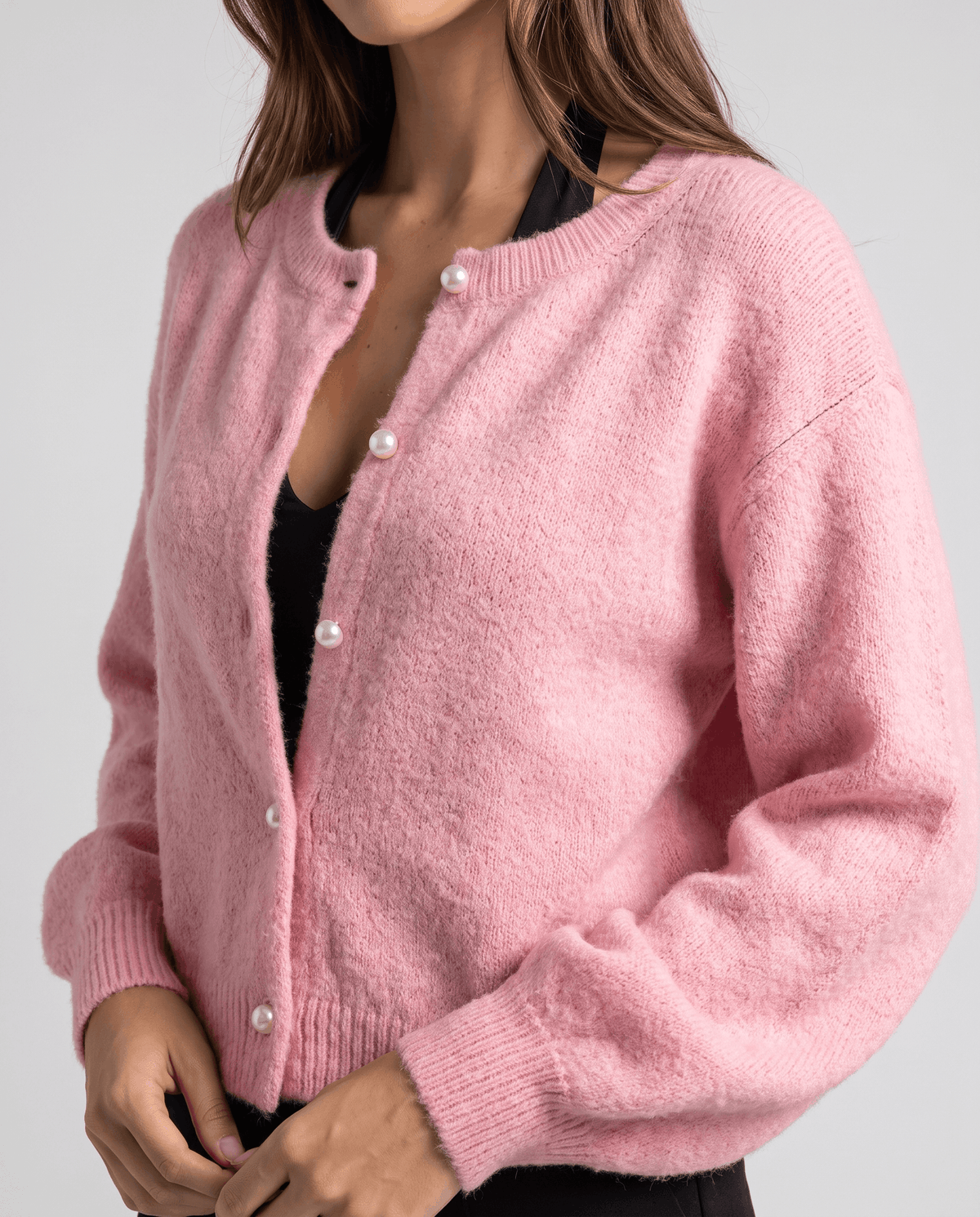 Pink knit cardigan worn partly unbuttoned over a black top, angled front view