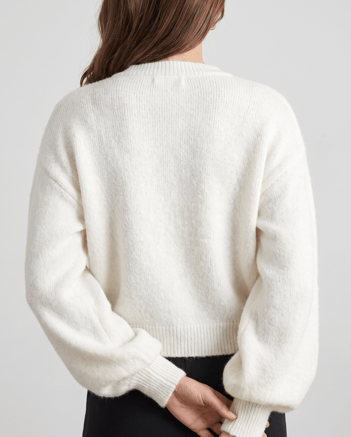 Back view of the white knit cardigan showing balloon sleeves and a ribbed hem