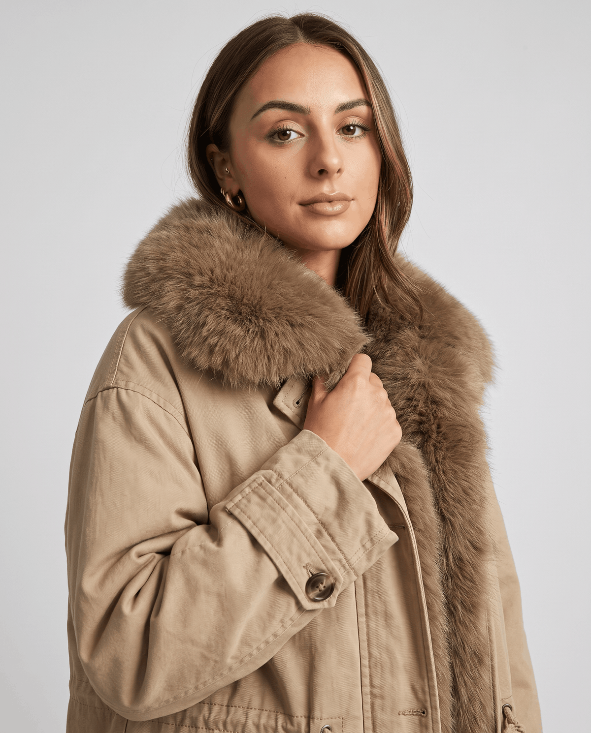 Model holding the plush collar of a khaki cotton parka