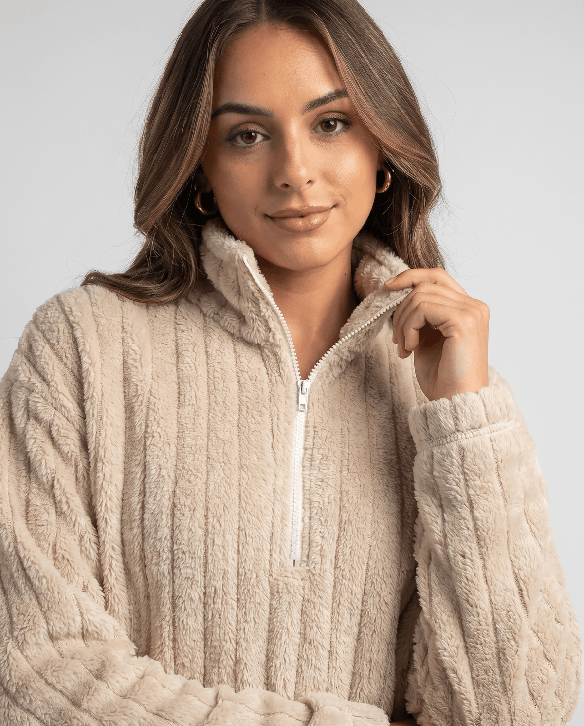 Close-up of model adjusting the stand collar and silver zip on a beige pullover