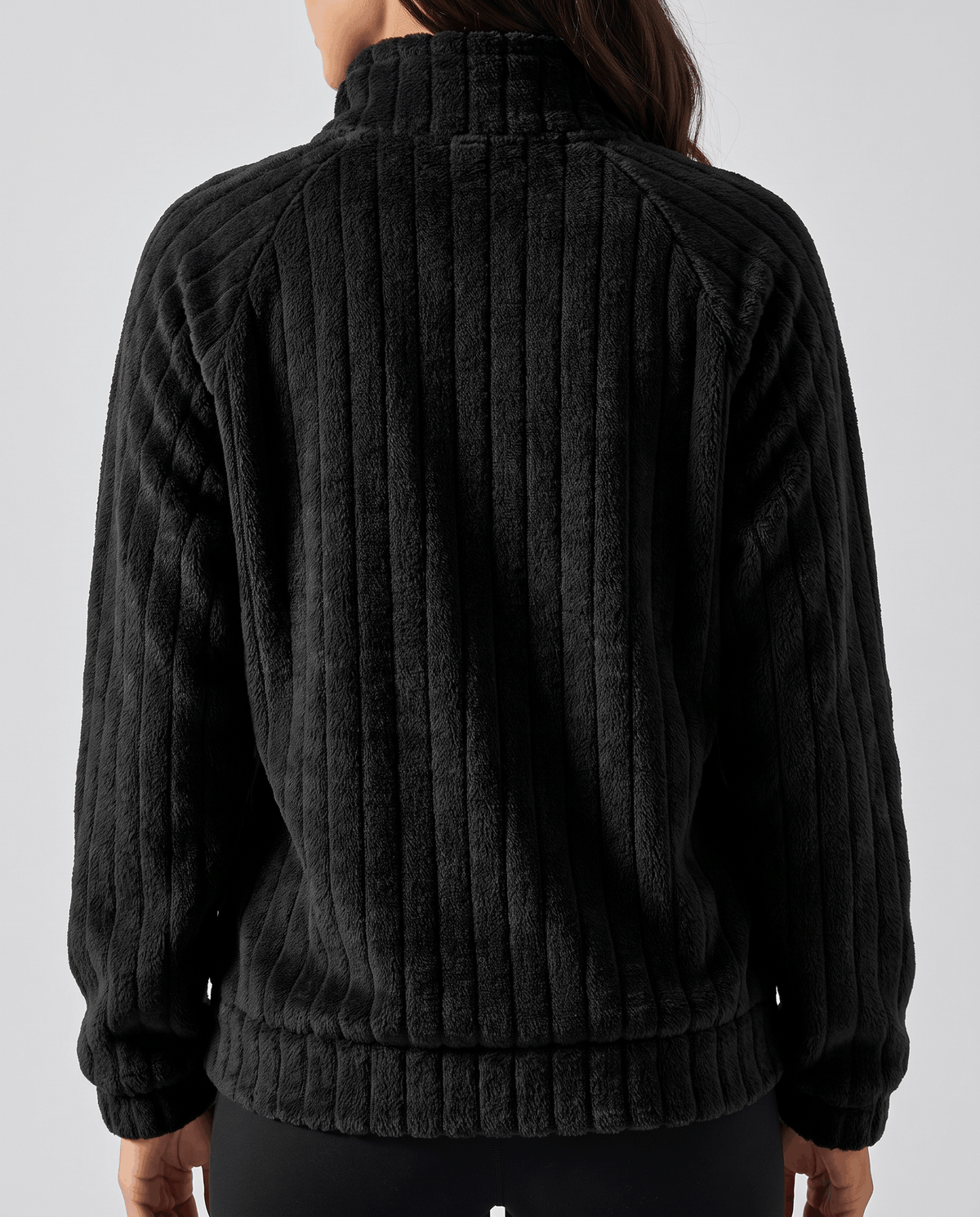 Back view of black plush pullover showing vertical ribs, banded hem and dark leggings