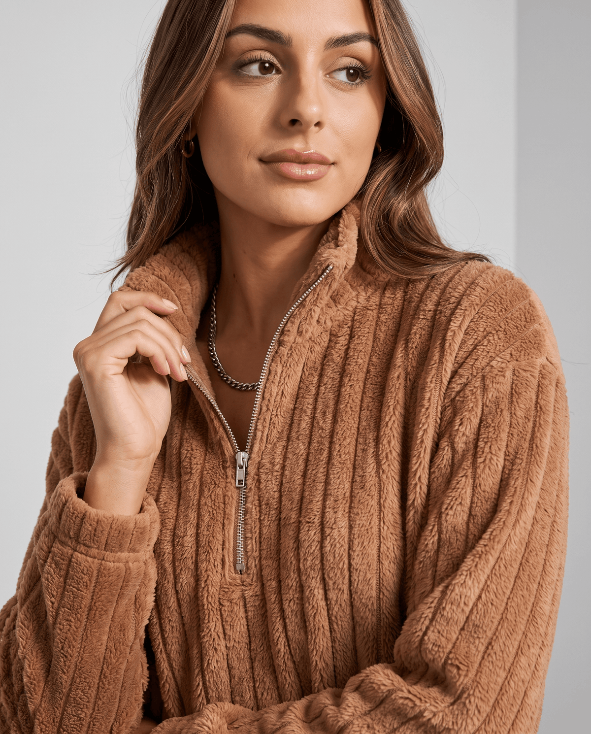 Model with hand at collar in a camel brown ribbed zip-neck pullover