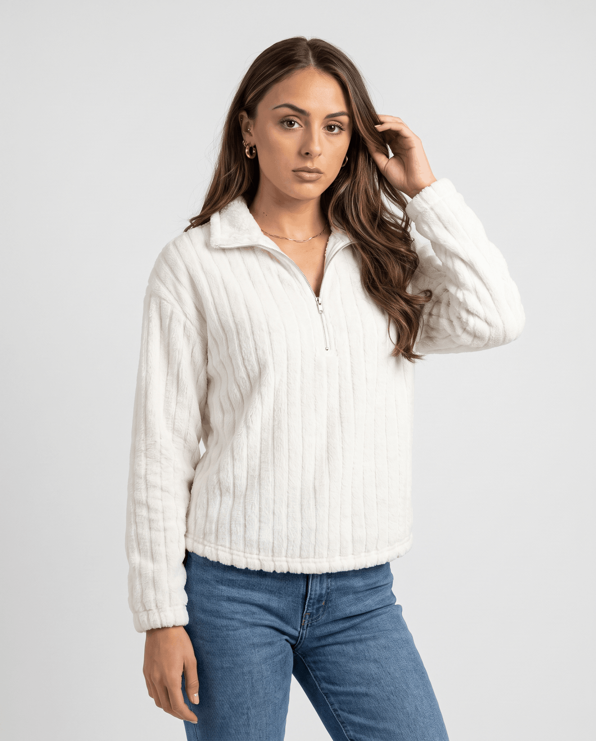 Model in white plush ribbed pullover and jeans, hand raised near the collar