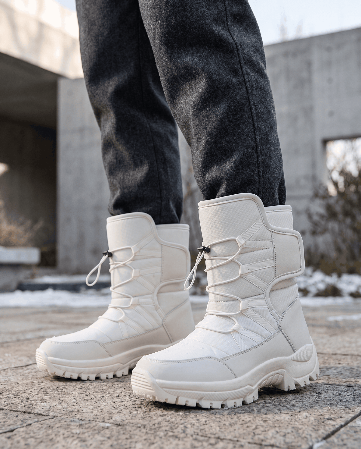 Man wearing beige quilted boots with dark trousers outdoors near a stone wall