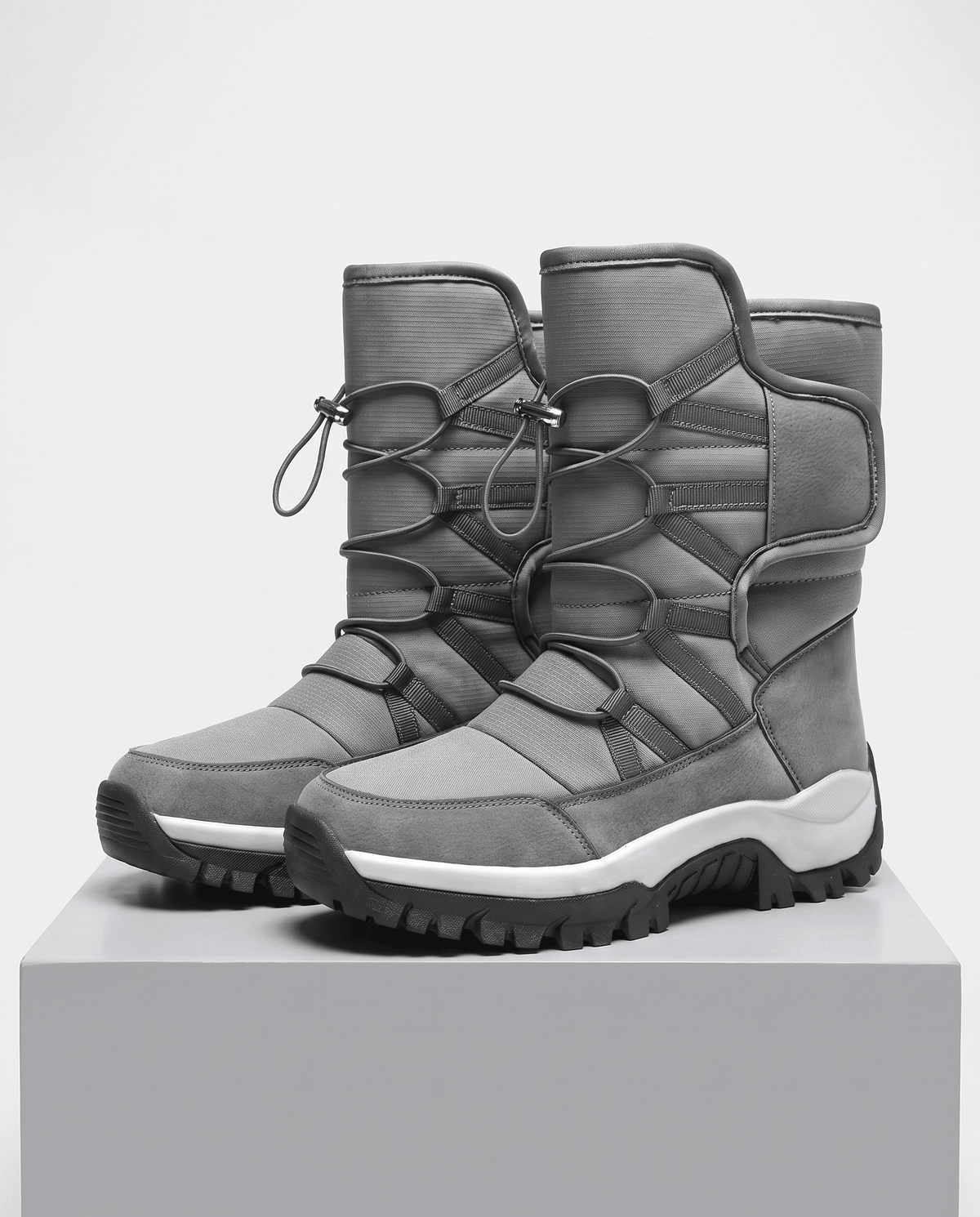Gray quilted mid-calf winter boots with drawstring tops and black lug soles on a plinth