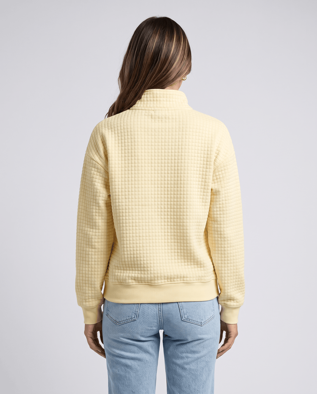 Back view of pale yellow quilted pullover worn with light wash jeans