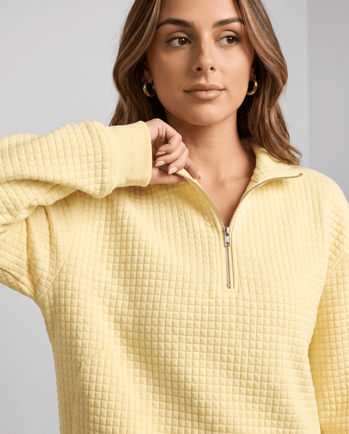 Close-up of model touching the stand collar and zip on a pale yellow pullover