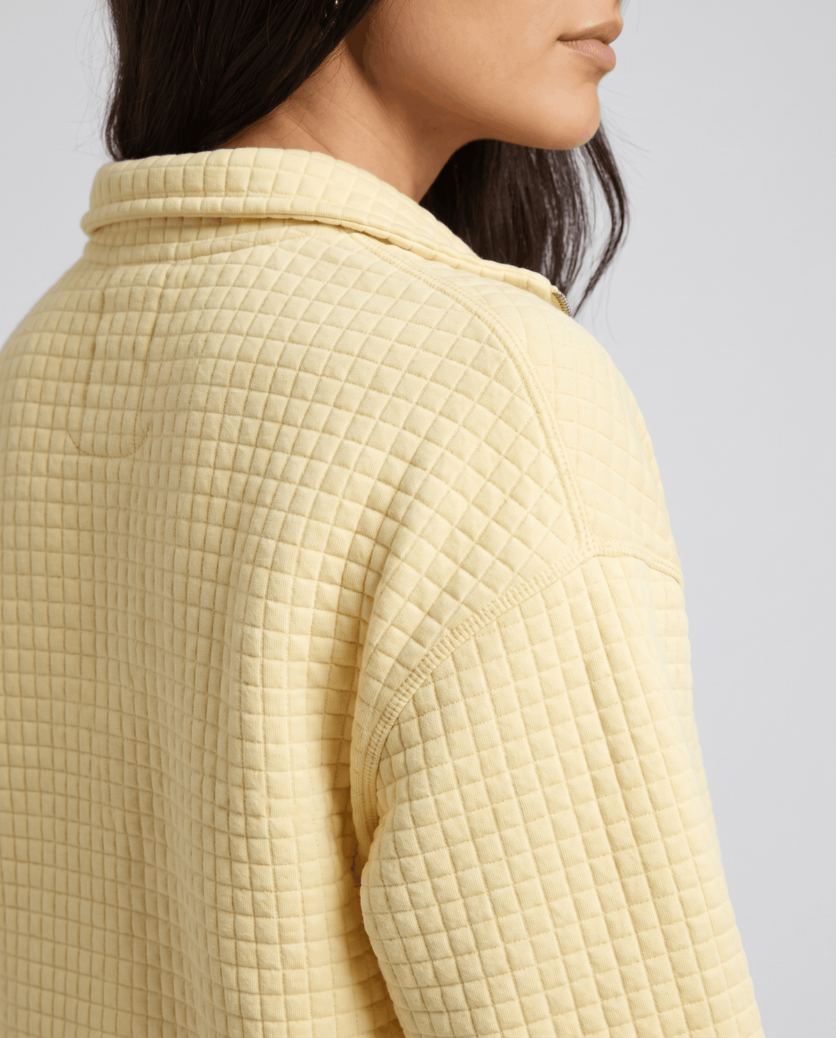 Shoulder detail showing square grid quilting on a soft yellow knit