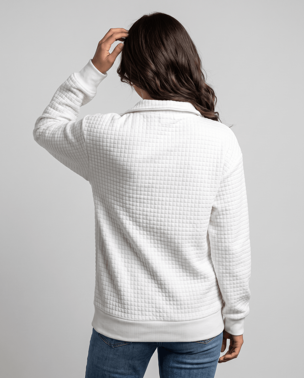 Back view of white quilted pullover with model lifting her hair
