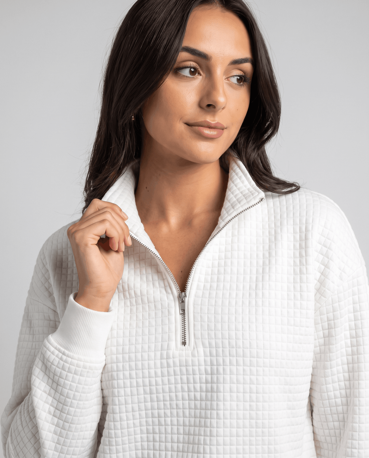 Model touching the zip collar of a white grid-textured pullover