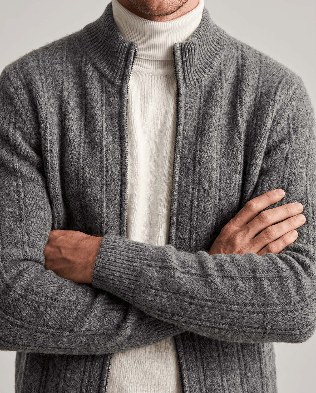 Gray ribbed cardigan worn open over a cream turtleneck, arms crossed