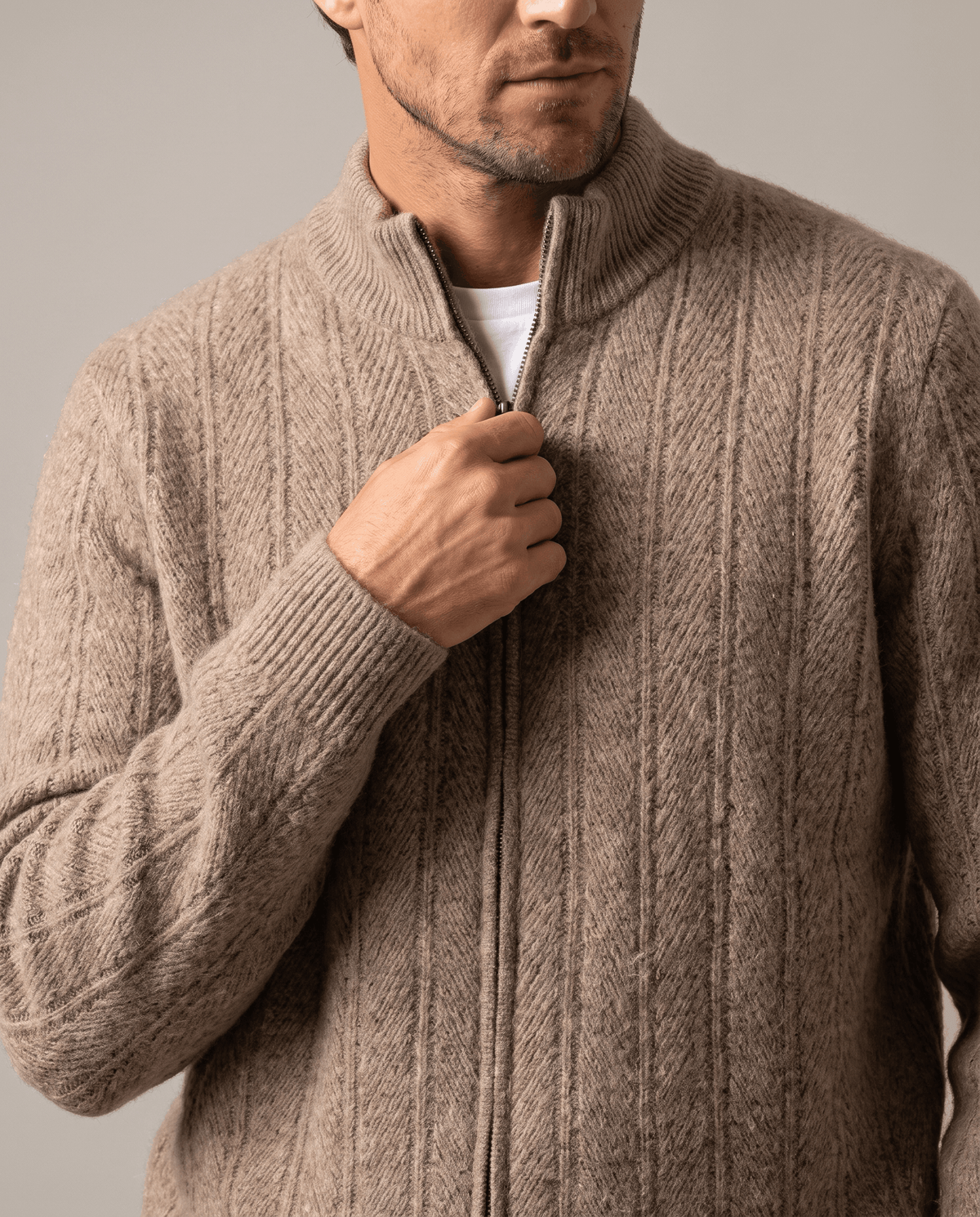 Close-up of a hand on the zip at the taupe cardigan's stand collar