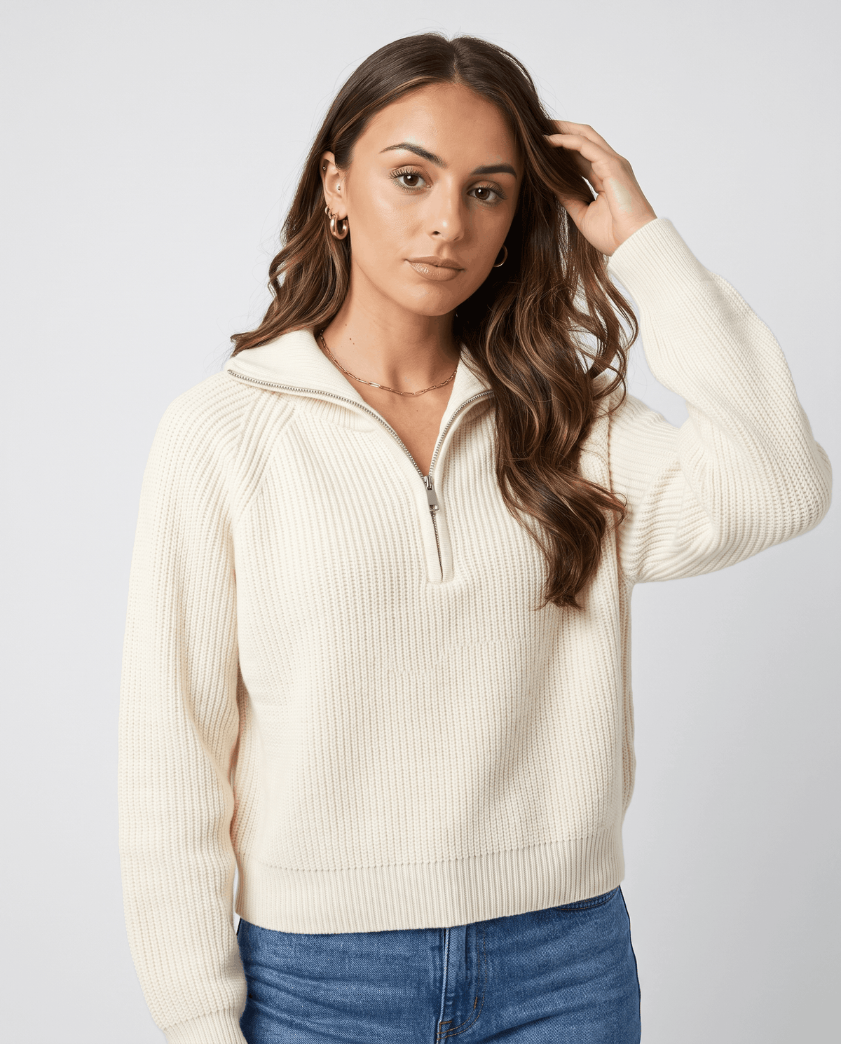 Model wearing the cream sweater with the collar up, hand in her hair