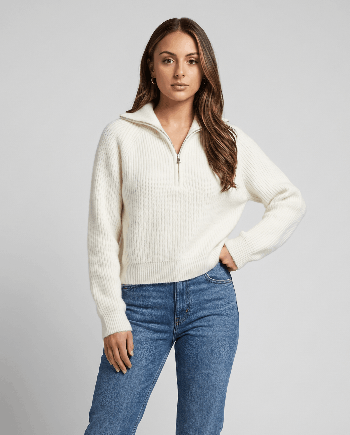 Woman in cream ribbed knit quarter-zip sweater with blue jeans, hand on hip